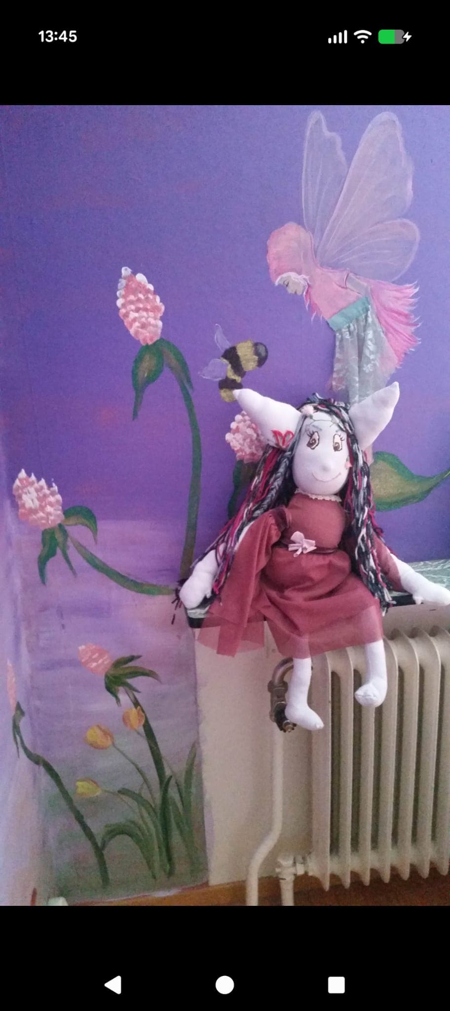 Blume doll against a wall of flowers